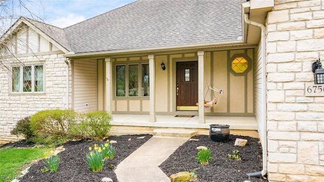 entrance to property with a porch, roof with shingles, and stone siding