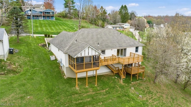 rear view of property featuring a sunroom, roof with shingles, a deck, and a lawn