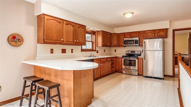 kitchen with a sink, brown cabinetry, a peninsula, and stainless steel appliances