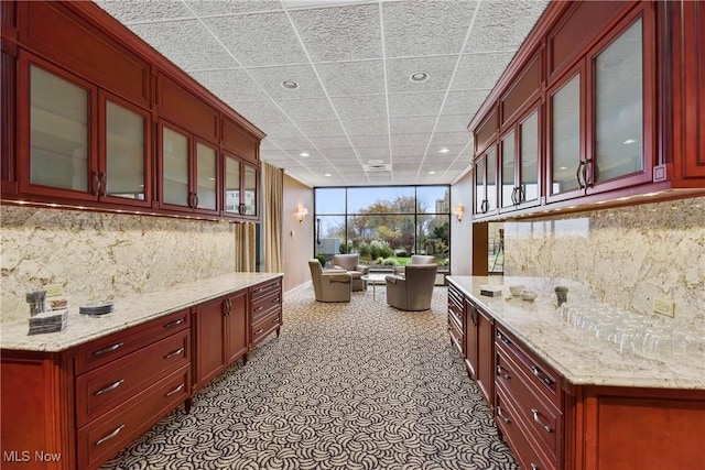 kitchen featuring dark brown cabinets, backsplash, glass insert cabinets, and light stone countertops