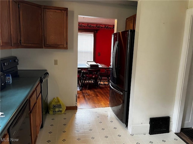 kitchen featuring visible vents, baseboards, light tile patterned floors, brown cabinetry, and black appliances