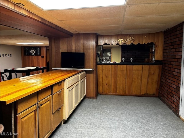 3265 Tieber Rd, Stockport, OH 43787 - kitchen featuring a paneled ceiling, light colored carpet, brown cabinets, brick wall, and wooden counters