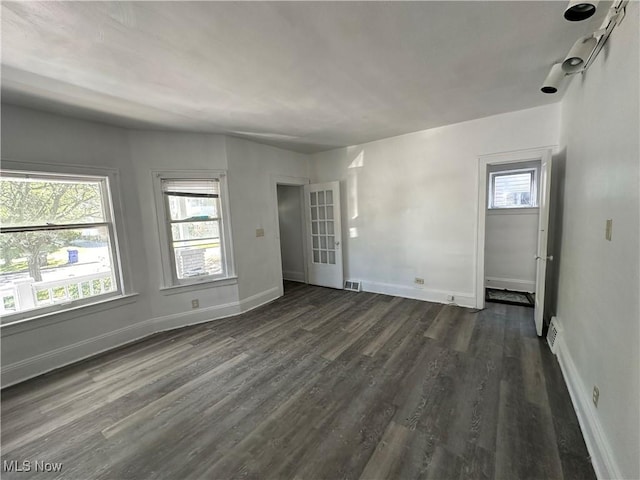 spare room with dark wood-type flooring, visible vents, and baseboards