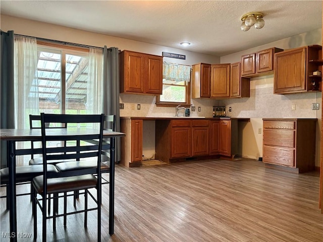 kitchen featuring open shelves, a sink, light wood-type flooring, brown cabinetry, and decorative backsplash