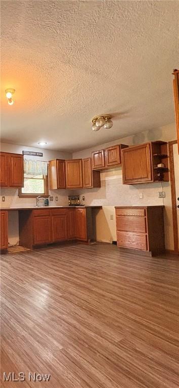 kitchen with brown cabinets, a textured ceiling, open shelves, and wood finished floors