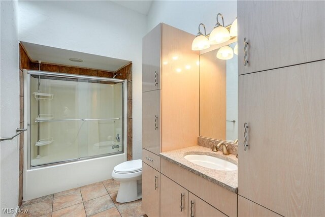 bathroom with combined bath / shower with glass door, tile patterned floors, vanity, and toilet