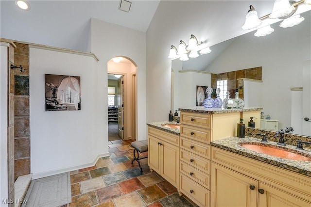 full bathroom with double vanity, vaulted ceiling, tiled shower, stone finish flooring, and a sink