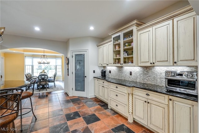 kitchen featuring arched walkways, decorative backsplash, baseboards, and cream cabinetry