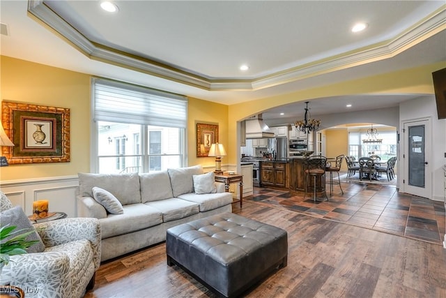 living room with ornamental molding, a tray ceiling, arched walkways, and a chandelier
