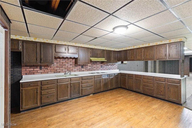 kitchen featuring light wood-style floors, white cooktop, under cabinet range hood, light countertops, and a sink
