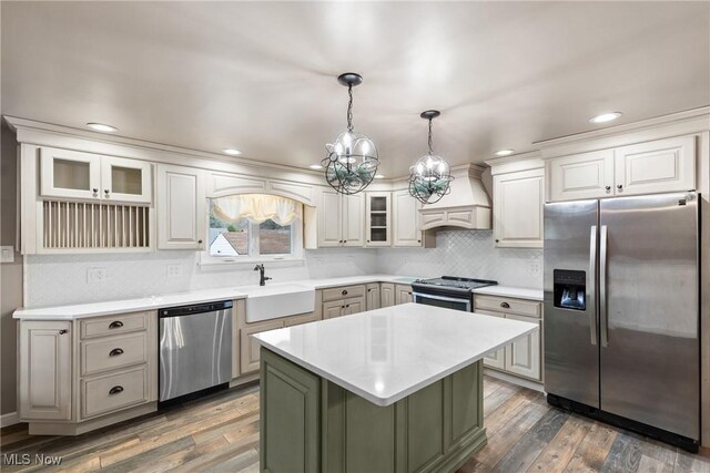 kitchen featuring custom exhaust hood, a sink, light countertops, appliances with stainless steel finishes, and wood finished floors