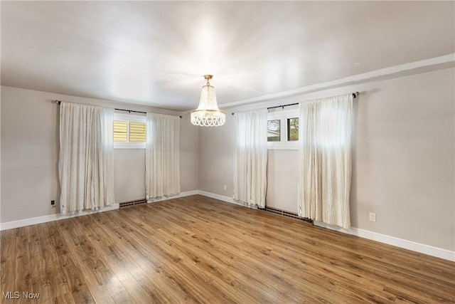 empty room with a chandelier, wood finished floors, baseboards, and a healthy amount of sunlight