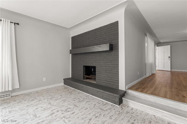 unfurnished living room featuring a fireplace with raised hearth, visible vents, baseboards, and wood finished floors