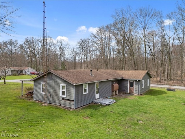 back of house with roof with shingles and a lawn