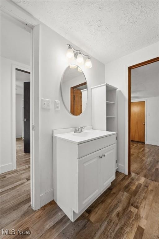 bathroom featuring a textured ceiling, wood finished floors, vanity, and baseboards