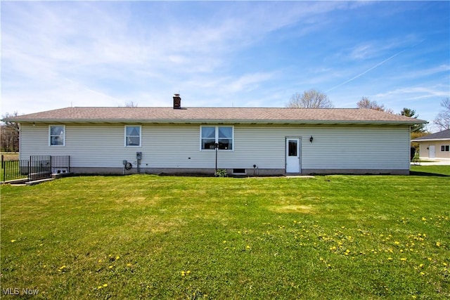 back of house featuring a lawn, a chimney, and fence