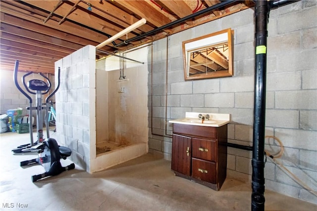 full bathroom featuring a stall shower, concrete block wall, unfinished concrete flooring, and vanity
