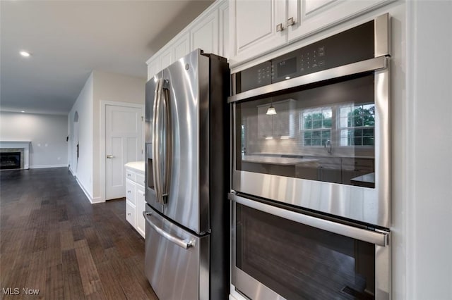 kitchen with a glass covered fireplace, baseboards, white cabinetry, dark wood finished floors, and stainless steel appliances