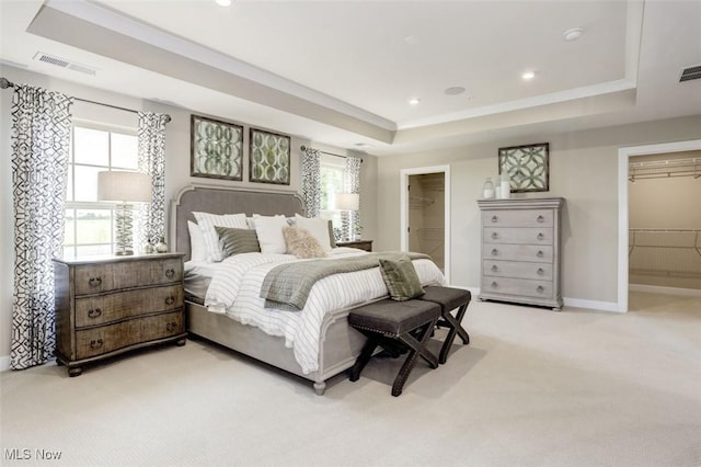 bedroom featuring visible vents, a walk in closet, a tray ceiling, and light carpet