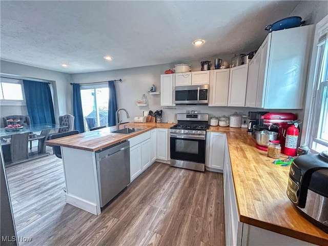 kitchen with a peninsula, dark wood-style floors, wooden counters, stainless steel appliances, and a sink