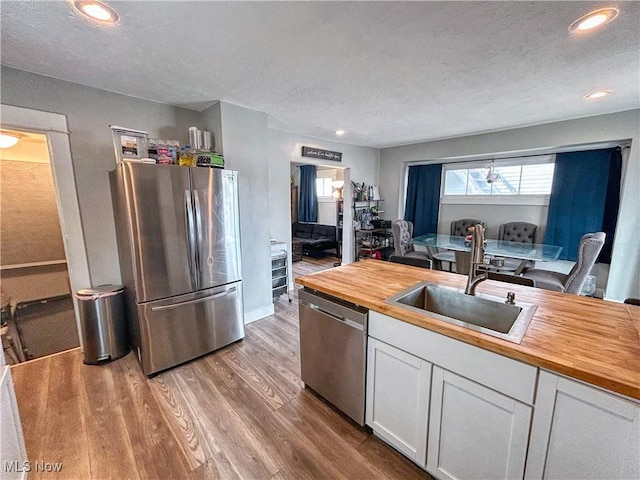 kitchen with wood counters, white cabinetry, a sink, and appliances with stainless steel finishes