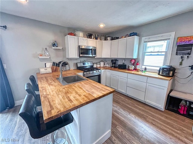 kitchen with a peninsula, wooden counters, white cabinets, appliances with stainless steel finishes, and a sink