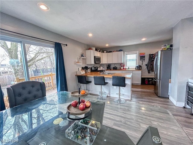 kitchen with light wood-style flooring, a peninsula, white cabinets, stainless steel appliances, and butcher block countertops