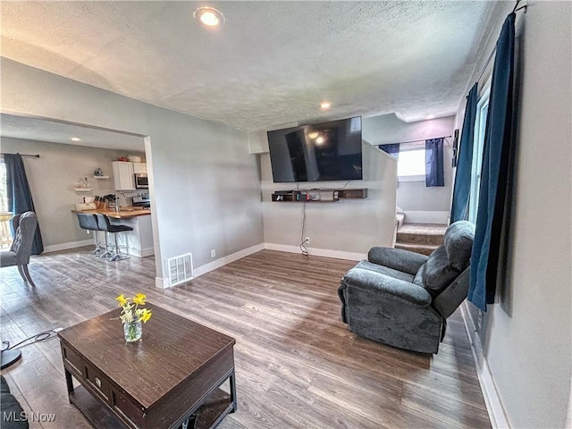 living area with visible vents, baseboards, a textured ceiling, stairway, and wood finished floors