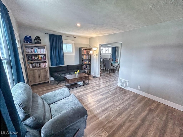 living area with a textured ceiling, wood finished floors, baseboards, and visible vents