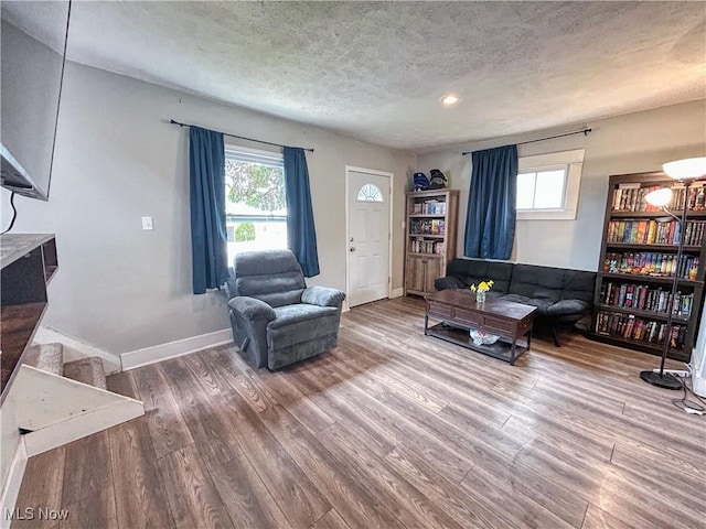 living area featuring a textured ceiling, baseboards, and wood finished floors