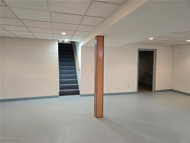 finished below grade area featuring baseboards, concrete block wall, a paneled ceiling, and stairway