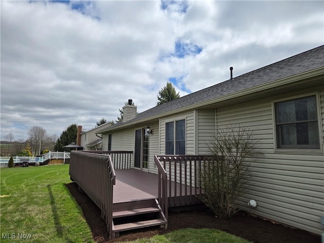 rear view of property featuring a deck, a chimney, and a lawn