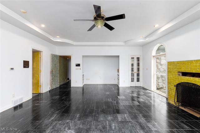 unfurnished living room with a fireplace, a ceiling fan, recessed lighting, a raised ceiling, and baseboards