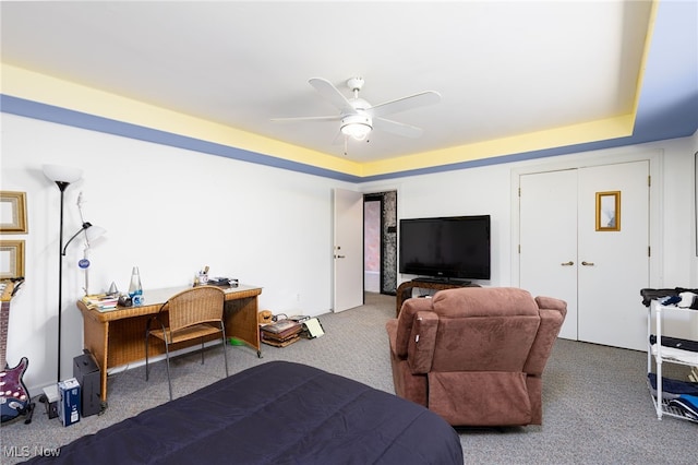 carpeted bedroom with a raised ceiling and ceiling fan