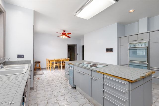 kitchen featuring tile countertops, white appliances, a center island, a sink, and gray cabinetry