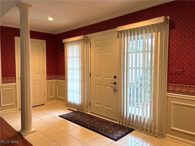 foyer entrance featuring a wainscoted wall, ornate columns, wallpapered walls, and crown molding