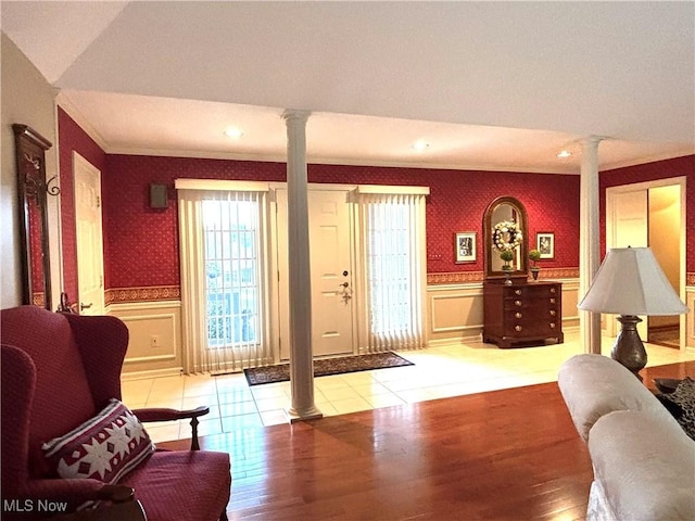 living room featuring ornamental molding, a wainscoted wall, decorative columns, and wallpapered walls