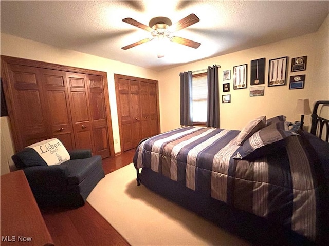 bedroom featuring a textured ceiling, multiple closets, a ceiling fan, and wood finished floors