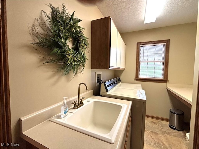 laundry area featuring baseboards, a textured ceiling, cabinet space, washer and dryer, and a sink