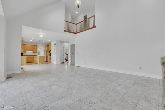 unfurnished living room featuring recessed lighting, stairway, a high ceiling, and baseboards