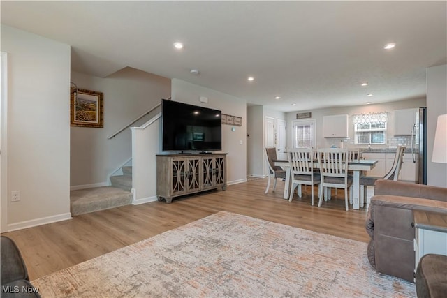 living room featuring baseboards, light wood finished floors, recessed lighting, and stairs