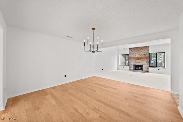unfurnished living room with visible vents, light wood finished floors, a chandelier, and a fireplace