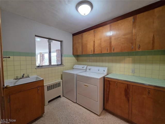 washroom featuring washing machine and clothes dryer, radiator heating unit, cabinet space, tile walls, and a sink