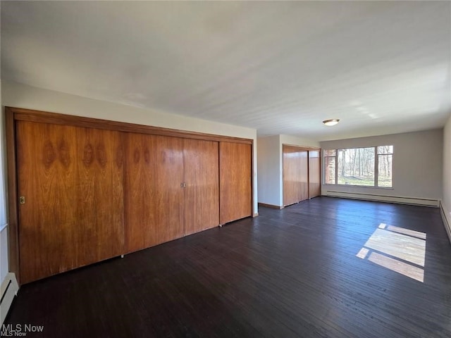 unfurnished living room with baseboard heating, a baseboard radiator, baseboards, and dark wood-style floors