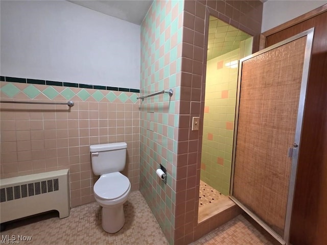 bathroom featuring radiator, tiled shower, a wainscoted wall, toilet, and tile walls