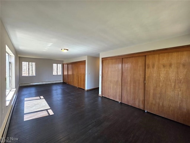 unfurnished living room with dark wood-style flooring, a baseboard radiator, and baseboards