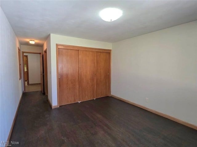 unfurnished bedroom with dark wood-style flooring, a closet, and baseboards