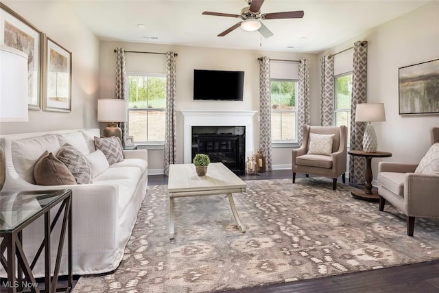 living area featuring a wealth of natural light, ceiling fan, a glass covered fireplace, and wood finished floors