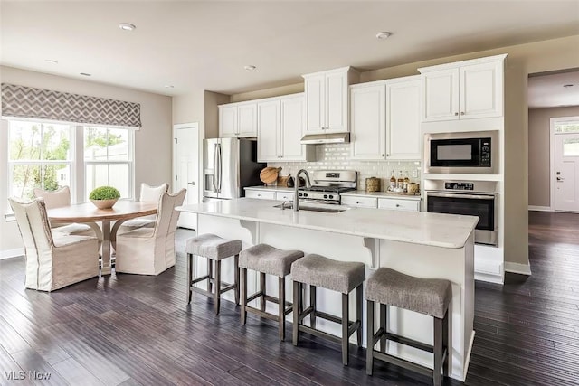 kitchen featuring white cabinetry, under cabinet range hood, light countertops, a sink, and stainless steel appliances