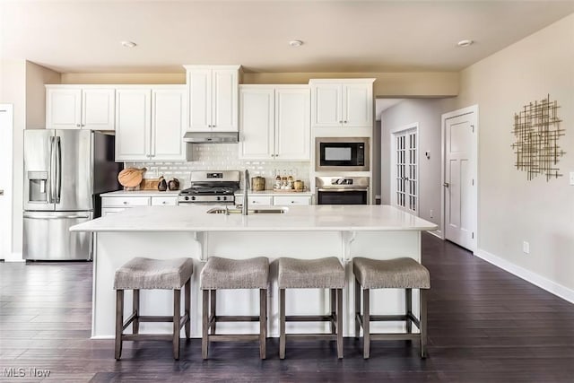kitchen with a sink, appliances with stainless steel finishes, a kitchen breakfast bar, and under cabinet range hood